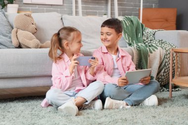 Cep telefonu ve tabletle evde video oyunları oynayan şirin, mutlu çocuklar.