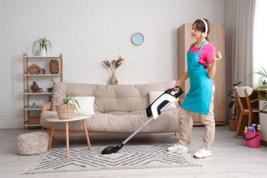 Kulaklıkları ve elektrikli süpürgesi olan güzel bir kadın evde halı temizlerken müzik dinliyor.