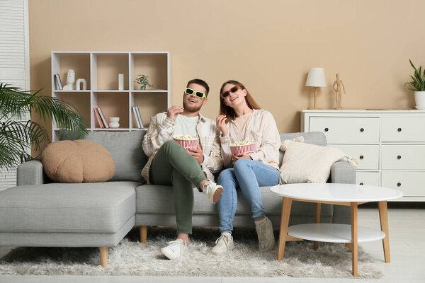 Счастливая молодая пара в 3D очках с ведрами попкорна смотреть кино на диване дома