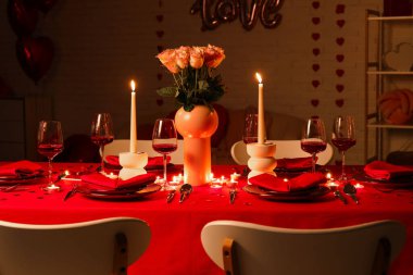 Akşamki Sevgililer Günü kutlaması için yemek masası, yanan mumlar ve pembe güller.