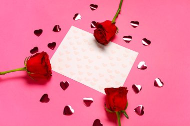 Kalpleri olan boş bir kart ve pembe arka planda kırmızı güller. Sevgililer Günü kutlaması