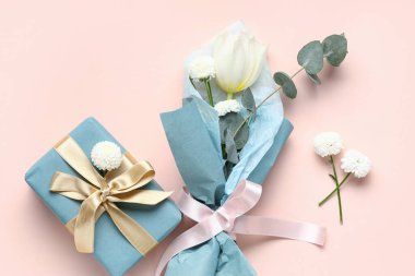 Pembe arka planda hediye kutusuyla ambalaj kağıdına sarılmış küçük bir buket güzel bahar çiçeği. Uluslararası Kadınlar Günü