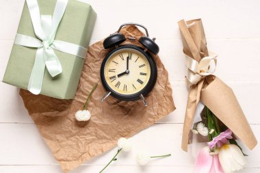 Hediye kutusu ve beyaz ahşap arka planda çalar saati olan ambalaj kağıdına sarılı küçük bir buket güzel bahar çiçeği. Uluslararası Kadınlar Günü