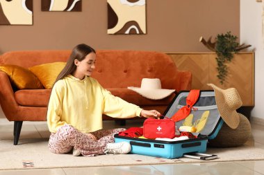 Evinde yerde oturan bavulu ve ilk yardım çantasıyla mutlu genç bir kadın. Seyahat kavramı