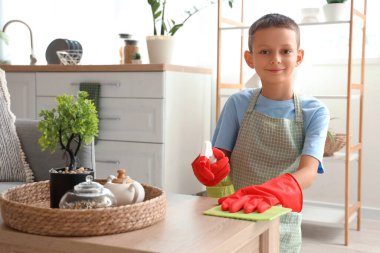 Paçavra ve spreyle evde kahve masasını temizleyen sevimli bir çocuk.