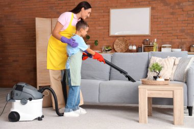 Anne oğluna elektrikli süpürgeyi evde nasıl kullanacağını öğretiyor.