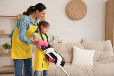 Anne kızına elektrik süpürgesini evde nasıl kullanacağını öğretiyor.