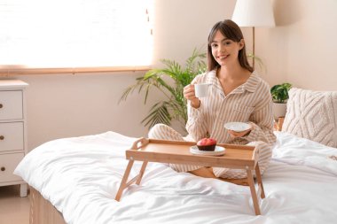 Pijamalı, elinde kahve ve kekle evde kahvaltı eden genç ve güzel bir kadın.