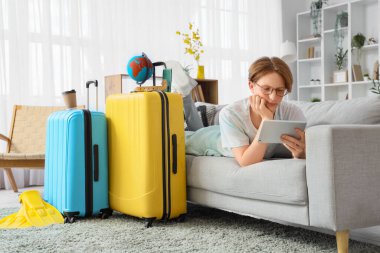 Tablet bilgisayarlı erkek turist, evdeki kanepede otel odası rezervasyonu yapıyor.