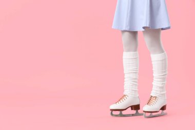 Pembe arka planda buz pateni yapan genç bir kadının bacakları.