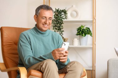 Cep telefonlu yaşlı adam evdeki koltukta oturuyor.