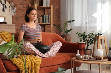 Evdeki kırmızı koltukta glukofon çalan genç bir kadın.