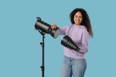 Mavi arka planda profesyonel ekipmanı olan Afro-Amerikalı bir fotoğrafçı.