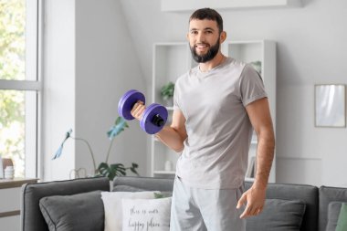 Sportif genç adam evde dambılla egzersiz yapıyor.