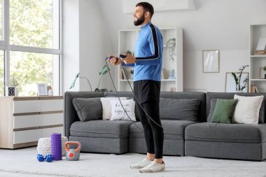 Sportif genç adam evde ip atlama egzersizi yapıyor.
