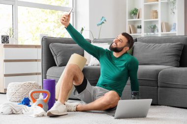 Laptoplu ve spor aletli genç adam evde selfie çekiyor.