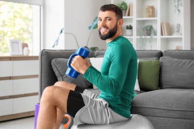 Spor salonundaki genç adam evde dambıllarla egzersiz yapıyor.