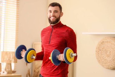 Sportif genç adam evde dambıllarla egzersiz yapıyor.