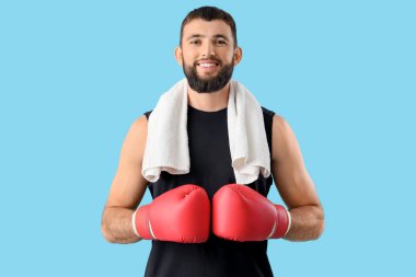 Mavi arka planda boks eldivenleri ve havlusu olan genç bir adam.