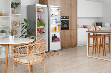 Ev bitkileriyle dolu modern mutfak ve taze yiyeceklerle dolu açık buzdolabı.