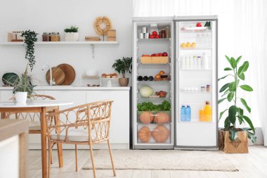 Ev bitkileriyle dolu modern mutfak ve taze yiyeceklerle dolu açık buzdolabı.