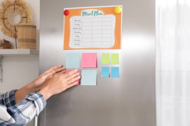 Modern mutfaktaki buzdolabına yapışkan notlar yapıştıran kadın.