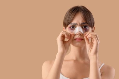 Bej arka planda sargılı burnu olan güzel, endişeli genç bir kadın. Estetik ameliyat konsepti