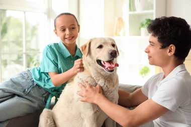 Mutlu kız ve erkek kardeş ve şirin Labrador köpeği evdeki kanepede oturuyor.