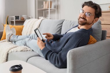 Evdeki kanepede e-okuyuculu genç bir adam yatıyor.