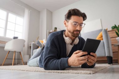 Evde yerde yatan e-okuyuculu genç adam.