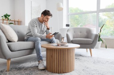 E-okuyuculu genç adam evdeki kanepede oturuyor.