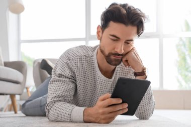 Evde yerde yatan e-okuyuculu genç adam.