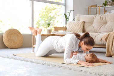 Küçük bebeğiyle evde yoga minderinde yatan sportif genç bir anne.