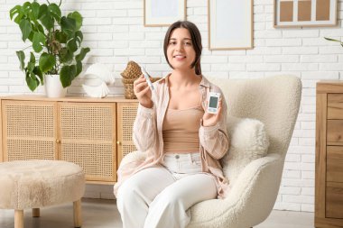 Glukometresi ve lambalı kalemi olan şeker hastası genç bir kadın evdeki koltukta oturuyor.