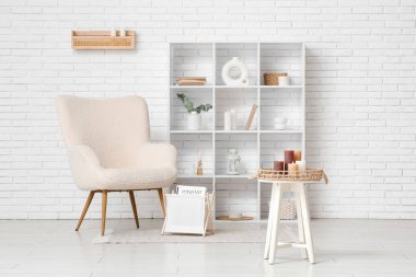 Rahat koltuk, dekorlu raf ünitesi ve hafif tuğla duvarın yanında yanan mumlar.