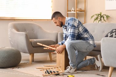 Genç adam evde ahşap masa kuruyor.