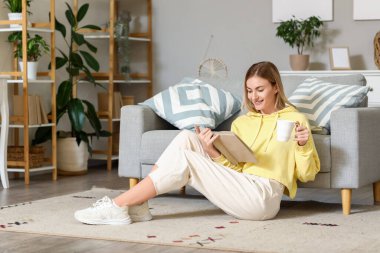 Evde halıda kitap okuyan genç bir kadın.