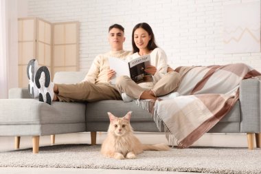 Dergisi olan güzel bir çift ve oturma odasında sevimli bir Maine Rakunu kedisi.