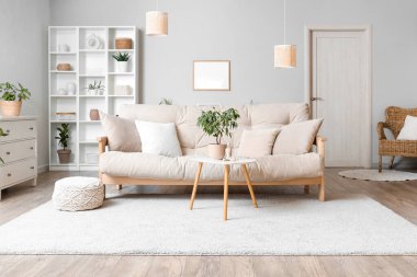 Oturma odasının içinde bej kanepe, masa ve raf ünitesi var.