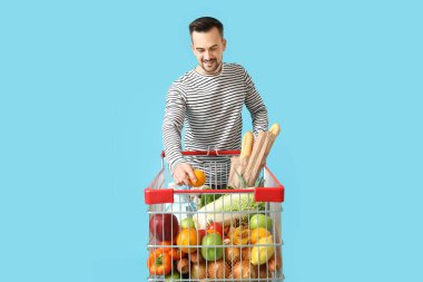 Mavi arka planda alışveriş arabası olan mutlu genç bir adam.