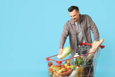 Mavi arka planda alışveriş arabası olan mutlu genç bir adam.
