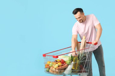 Mavi arka planda alışveriş arabası olan mutlu genç bir adam.