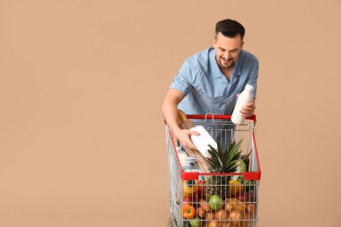 Tam alışveriş arabası ve bej arka planda bir şişe sütü olan mutlu genç bir adam.