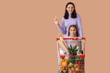 Güzel, genç, mutlu anne ve kızı bej arka plandaki bir şeyi işaret ediyorlar.