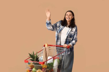 Güzel, genç, mutlu bir kadın. El sallıyor bej arka planda.