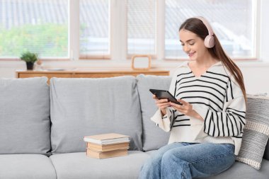 Kulaklıklı genç kız evde e-kitap okuyor.