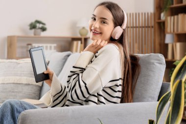 Kulaklıklı genç kız evde e-kitap okuyor.