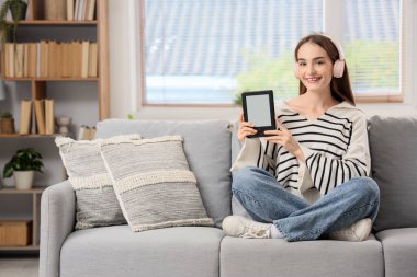 Evdeki kanepede oturan e-okuyuculu genç kız.