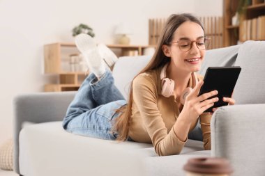 Evdeki kanepede uzanmış e-kitap okuyan genç bir kız.