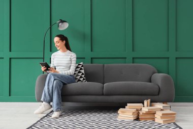 Evdeki kanepede oturmuş e-kitap okuyan genç bir kız.